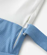 Vestido midi de la marca Ashua con parte superior de malla lisa en color blanco y falda de algodón con estampado de rayas verticales en azul y blanco. Posee mangas cortas, escote redondo y un lazo ajustable en la cintura.