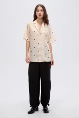 Camisa de lyocell color beige con estampado de lunares negros, cuello solapa, manga corta y cierre frontal con botones.