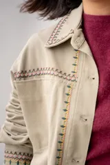 Campera de jean color beige con bordados florales en tonos rosa, verde y amarillo.