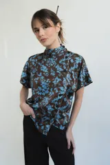 Blusa de seda con estampado floral en tonos marrón y celeste, con cuello alto, manga corta japonesa y cierre cruzado con botones negros visibles en diagonal.