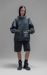 Hoodie oversize de algodón con diseño bicolor en gris oscuro y gris medio. Presenta capucha forrada, mangas raglán con recortes técnicos y un bolsillo frontal tipo canguro con un compartimento adicional con solapa.