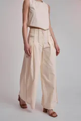 Pantalón marrón de corte palazzo, tiro alto, con pliegues frontales y pespuntes blancos decorativos.