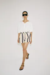 Shorts de tiro medio con trabillas en la cintura y cierre frontal con cremallera y botón. Presenta pliegues delanteros y bolsillos laterales ocultos en la costura, con un diseño de rayas verticales multicolor.