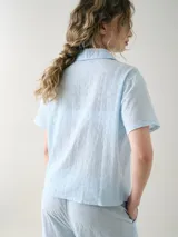 Camisa de manga corta para dormir confeccionada en broderie de algodón, con cuello solapa y cierre frontal con botones. Presenta un bolsillo aplicado en el pecho.