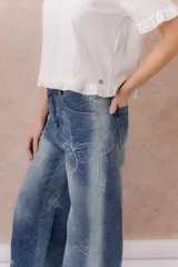 Jean de tiro medio y pierna amplia, con calce wide leg y lavado azul con efecto desgastado. Presenta estampado floral y de mariposas en toda la prenda, bolsillos delanteros y traseros, y cierre frontal.