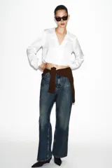 Camisa corta de tejido satinado color marrón, con cuello solapa, escote en pico y manga larga. Presenta cierre frontal con botones forrados a tono.