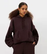 Hoodie de color marrón oscuro con diseño voluminoso tipo globo, capucha con cordón de ajuste, mangas largas abullonadas con pliegues y bolsillo canguro frontal.