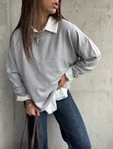 Sweater de punto color gris, de corte holgado y diseño de manga larga con costuras visibles en los hombros. Presenta cuello redondo y puños acanalados.