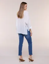 Camisa blanca de silueta holgada y textura liviana, con cuello camisero clásico, abotonadura frontal con botones en contraste y doble bolsillo de parche en el frente. Cuenta con mangas de corte dolman de largo tres cuartos con puño amplio y ruedo recto con aberturas laterales.