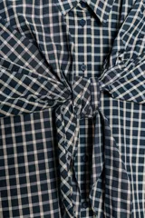 Camisa oversize de algodón con estampado de cuadros, cuello solapa, manga larga con puños y cierre frontal con botones. Presenta un detalle de pañuelo integrado en el mismo tejido que se anuda en la parte frontal.