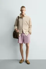 Bermuda de hombre con corte relaxed fit, tiro medio, cintura elástica con botón y cierre de cremallera. Presenta un patrón de cuadros pequeños en tonos rosados y grises.