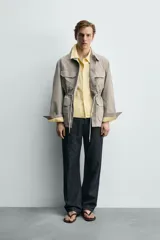 Parka relaxed fit color gris, confeccionada en tejido técnico ligero, con cuello solapa, manga larga con puño abotonado, cuatro bolsillos de plastrón con solapa en el frente, cintura ajustable con cordón y cierre frontal de botones.