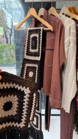 Bufanda con capucha integrada, tejida a mano en crochet con diseño de cuadrados tipo granny square en tonos negro, blanco y marrón.