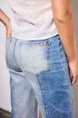 Jean de tiro medio, corte recto y largo cropped, confeccionado en denim de algodón con elastano. Presenta un efecto de lavado bicolor o combinado, con paneles de diferente tono de azul claro, y costuras verticales marcadas en el frente. El ruedo es deshilachado.
