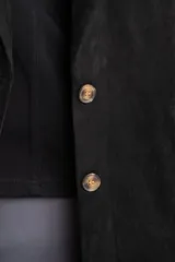 Blazer negro de textura gamuzada con solapas clásicas, cierre frontal de dos botones y bolsillos laterales con solapa.