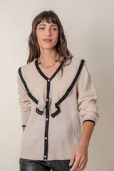 Cárdigan negro de punto fino con hilos de lurex, cuello en V calado con volados color crema, cierre frontal con botones con strass y puños anchos con ribete color crema.