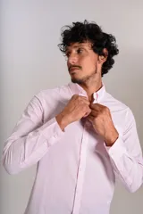 Camisa de manga larga confeccionada en tejido poplin con diseño de rayas verticales finas en color rosado y blanco. Presenta cuello abotonado (button-down), cierre frontal con botones y un bolsillo en el pecho.