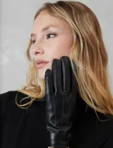 Guantes de cuero sintético color negro, con costuras decorativas en el dorso y detalle de tira con broche a presión en la muñeca. Interior forrado en terciopelo.