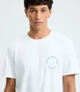 Remera de hombre modelo comfort, color blanco, confeccionada en media malla de algodón y poliéster. Presenta cuello redondo, manga corta y un pequeño estampado circular en el pecho con texto en color celeste.