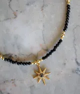 Collar de cuentas negras y doradas con dije de estrella en baño de oro, adornado con circonitas blancas y azules.