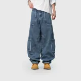 Pantalón de jean estilo cargo con corte ultra baggy y diseño de paneles. Presenta bolsillos laterales tipo cargo con bordes deshilachados y costuras reforzadas. Confeccionado en denim de algodón con textura rústica.