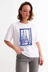 Remera blanca de manga corta con estampa frontal en color azul que representa una ventana abierta con vista a la Torre Eiffel y la inscripción Paris, France 1996.