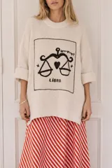 Sweater de punto negro de corte oversize, con cuello redondo y diseño bordado a mano en color crudo en el frente que representa el signo de Acuario con la figura de una sirena y estrellas.