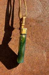 Collar con cordón de cuero y dije alargado de piedra verde con detalles translúcidos y casquillo metálico dorado.