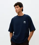 Remera de corte oversized color azul marino, con cuello redondo y mangas cortas. Presenta un estampado gráfico grande en la espalda con el texto 'Innovation Research' y diversos elementos visuales de estilo tecnológico.
