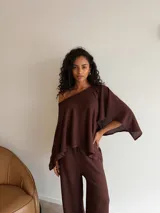 Blusa de tejido waffle color marrón, con diseño asimétrico de un solo hombro y mangas anchas tipo capa.