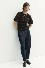 Camisa de cuello redondo y manga corta abullonada, con diseño de cuadros en tonos negro y marrón. Presenta un cuerpo entallado mediante frunces elásticos en la cintura y cierre posterior con abertura y botón.