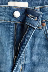 Jean de tiro alto confeccionado en denim de algodón con leve elasticidad. Presenta diseño de cinco bolsillos, cierre frontal con botón y cremallera, y perneras amplias de corte holgado con bajo deshilachado.