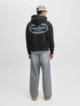 Buzo con capucha y manga larga, fit holgado, color negro. Confeccionado en tejido de punto circular loopback 100% algodón con interior cepillado. Presenta un estampado ovalado en la espalda con texto en blanco que incluye "ESTABLISHED IN COPENHAGEN 1990", "JACK&JONES WORLDWIDE MRK", "ORIGINALS CREATIVE DEPARTMENT DAILY BASICS" y "FROM VISION TO REALITY".