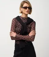 Blusa de manga larga confeccionada en tul semitransparente, con estampado de lunares blancos sobre base marrón, cuello alto y diseño ajustado al cuerpo.