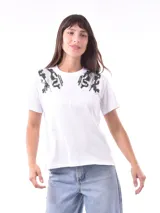 Remera blanca de manga corta con cuello redondo, destacada por apliques bordados con lentejuelas en los hombros.