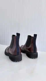Botín tipo Chelsea de cuero color bordó, con paneles laterales elásticos negros y detalle de tira vertical en gamuza azul marino en el talón. Cuenta con suela track robusta de goma negra.