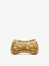 Bolso de mano tipo clutch con forma curva y acabado brillante, estampado con un patrón de patitos amarillos. Posee un cierre frontal metálico con el logo de la marca.