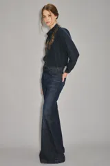 Jean de corte acampanado estilo setentero, confeccionado en denim azul oscuro. Presenta una cintura con detalle de trenzado integrado y un calce ajustado en la parte superior que se ensancha desde la rodilla hacia abajo.