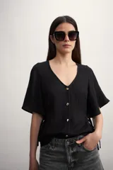 Camisa negra con botones dorados, escote en V y mangas cortas amplias con lazos laterales. 