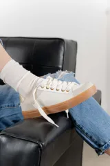 Zapatillas color marfil con detalles dorados en el talón y ojales metálicos. Suela de goma caramelo y cordones beige.