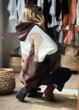 Campera tipo hoodie de textura tipo corderito, con diseño de paisaje montañoso en bloques de color marrón, blanco y beige. Presenta capucha y un parche de cuero con logo en la parte posterior.