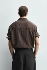 Camisa de corte relajado confeccionada en tejido ligero de algodón con textura de cuadros. Presenta cuello solapa, manga larga con puños abotonados y cierre frontal de botones.