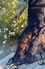 Falda larga de color azul marino confeccionada en microtul y gasa. Presenta un diseño con frunces y plisados en la zona de la cadera que brindan un ajuste al cuerpo, y una parte inferior fluida con transparencias y efecto godet.