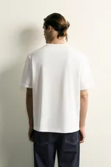 Camiseta relaxed fit color blanco, de cuello redondo y manga corta. Presenta un pequeño parche aplicado a contraste en el extremo de la manga y terminaciones en rib.
