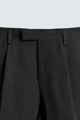 Pantalón de vestir negro con pliegues frontales, corte regular fit, bolsillos laterales y traseros de doble vivo con botón. Cierre frontal cruzado con cremallera y gancho metálico.