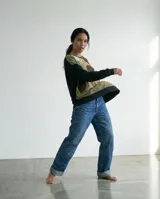 Remera tipo poncho de silueta amplia y relajada, confeccionada en una combinación de jersey y viscosa. Presenta un diseño bicolor con un panel frontal estampado con formas orgánicas en tonos tierra y verde, y mangas y espalda en color negro.