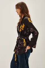 Saco tipo kimono de satén negro con estampado floral en tonos violeta y amarillo, con lazo ajustable en la cintura y mangas largas.