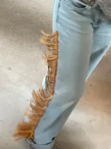 Pantalón de jean de corte recto y tiro medio, con detalle de flecos laterales largos en cuero genuino.
