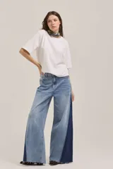 Pantalón de jean de corte wide leg con diseño bicolor, combinando un tono de denim claro en el frente y un panel lateral en denim azul oscuro. Presenta un acabado deshilachado en el ruedo.