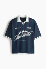 Camiseta de fútbol de manga corta en malla estampada, con diseño a rayas verticales en tonos azul y verde oscuro. Cuenta con cuello polo blanco y escote en V con ribete negro, además de estampados gráficos frontales con estrellas y la inscripción "Run Wild". Presenta un corte holgado.